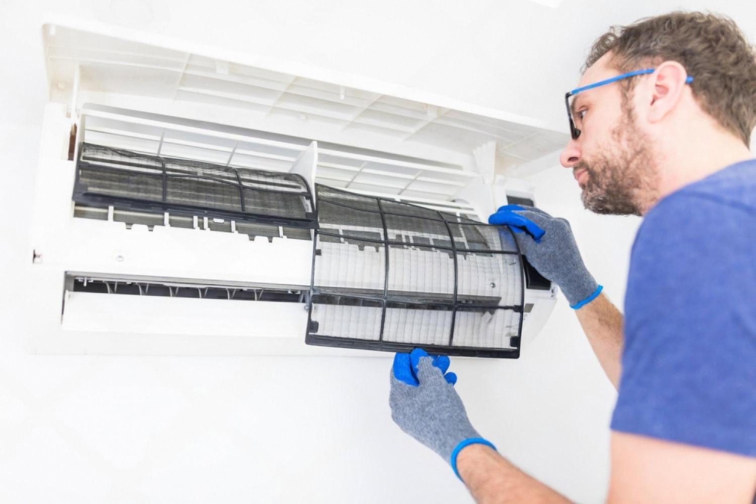 Technician in gloves removing a dusty filter from a split air conditioner for cleaning