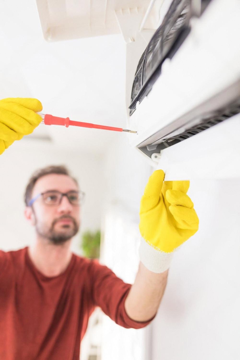 AC technician unscrewing an indoor air conditioner cover during routine servicing