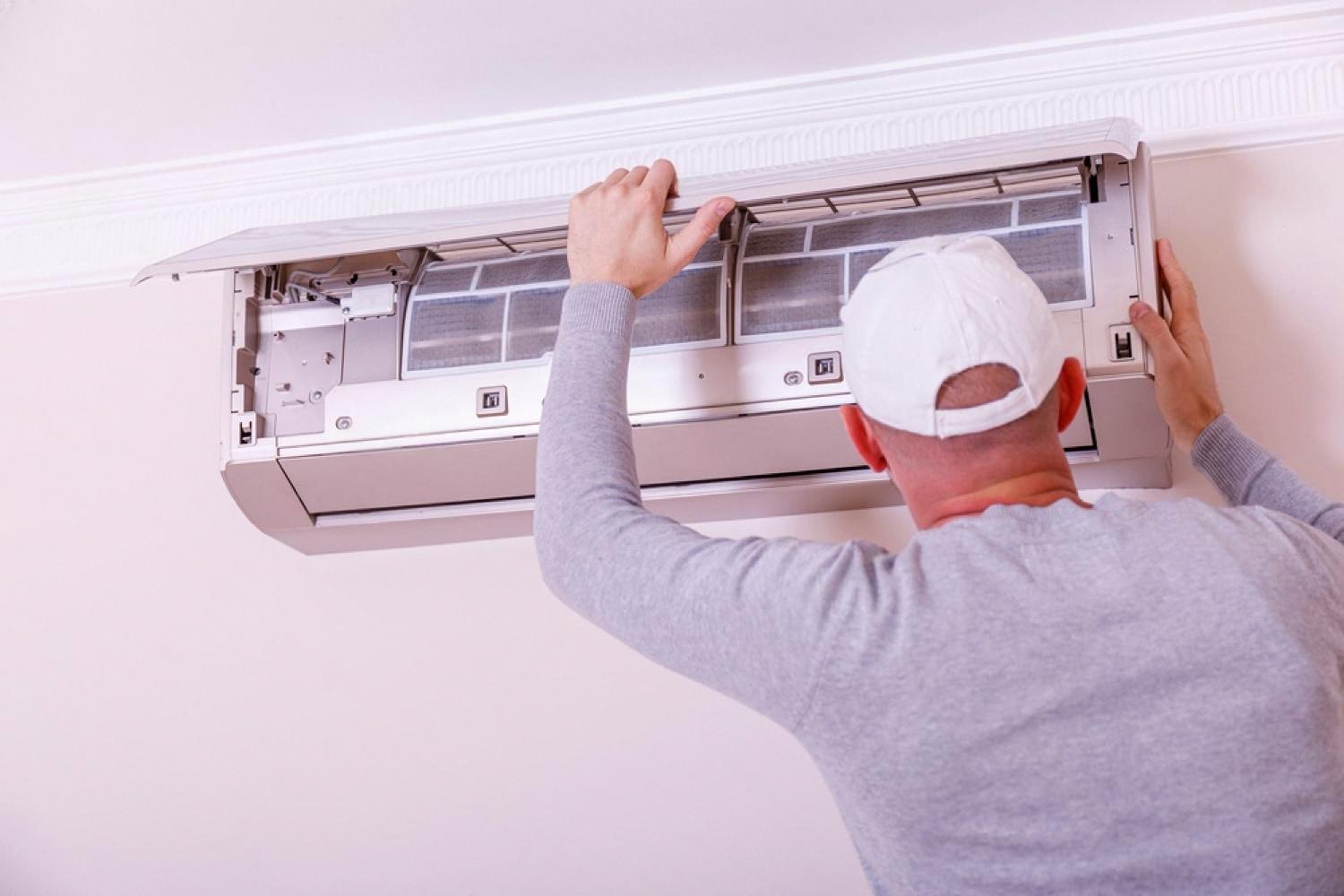 Homeowner opening the front panel of a wall-mounted AC unit to inspect the filters